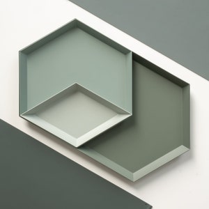 May include: Two hexagonal trays, one nested inside the other, are made of a light green metal. The trays are angled against a white background.