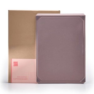 May include: A rectangular, mauve-colored cutting board with a geometric design, next to a cardboard box and a pink information card. The cutting board has a textured surface and decorative corner accents. The card reads "Geometric Cutting Board".