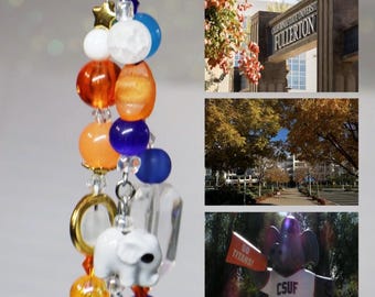 May include: A beaded keychain featuring a silver-tone lobster clasp, a white elephant charm, and a variety of round beads in orange, blue, white, and yellow. The design includes small star-shaped beads and clear spacers, hanging vertically.