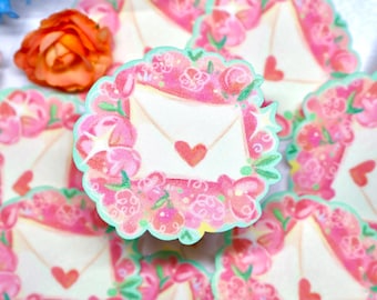 May include: A collection of circular stickers featuring a central cream-colored envelope with a red heart seal, surrounded by a vibrant wreath of pink and red flowers with green leaves and a scalloped light green border edge.