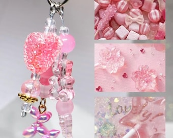 May include: A silver-toned keychain featuring a collection of pink charms, including a glittery heart, a translucent bear, and a balloon dog. The keychain is displayed alongside three rectangular image insets showing pink candies, flower-shaped lollipops, and a star-shaped lollipop with the word "lovely" printed on it.