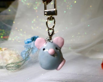 May include: A gray mouse-shaped charm attached to a silver-toned metal lobster clasp. The mouse features a smooth, rounded body, two light pink ears, a small pink nose, and two black dot eyes. The charm is suspended from a metal swivel hook.