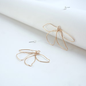 Puede incluir: Un par de pendientes de alambre dorado con forma de flor de cinco pétalos.