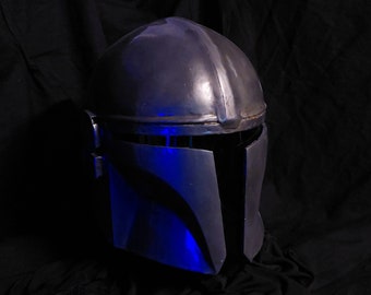 May include: A dark gray helmet with a blue light reflecting off of it. The helmet has a visor and a T-shaped design on the front.
