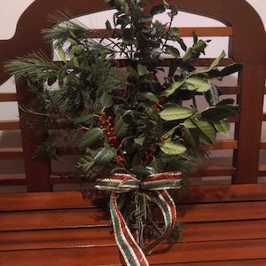 May include: A green and red Christmas swag with a red and green ribbon bow. The swag is sitting on a wooden bench.