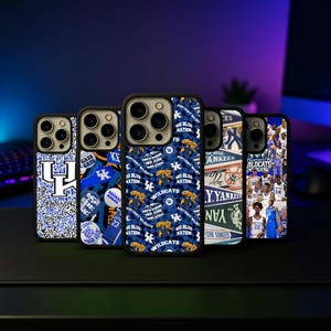 May include: A collection of phone cases with various designs. The cases feature a black border and a variety of graphics, including the Kentucky Wildcats logo, team colors, and the words "Big Blue Nation" and "Wildcats". One case displays a New York Yankees design.