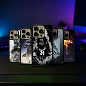 May include: A collection of phone cases featuring various designs. The cases showcase detailed artwork, including a skull-like figure, a warrior, and other graphic elements. The cases are black with a protective bumper.
