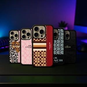 May include: A collection of five phone cases with various designs. The cases feature patterns like leopard print, pink Coach logo, brown and tan stripes, a red panel with "COACH NEW YORK" text, and a black textured design. Each case has a black border.