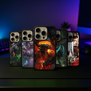 May include: A collection of phone cases with fantasy art designs. The cases feature various characters and creatures, including a dragon, warrior, and other fantasy figures. The cases have a black border and are displayed on a dark surface.