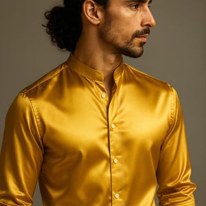 Op de afbeelding: Een goudgele satijnen blouse met een opstaande kraag en een knoopsluiting aan de voorkant. De blouse met lange mouwen heeft een glanzende glans en is gemaakt van een gladde, vloeiende stof. De blouse is een klassieke stijl.