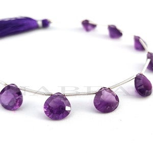 May include: A strand of purple amethyst gemstone beads, each bead is faceted and pear-shaped. The beads are strung on a silver wire and have purple tassels at either end.