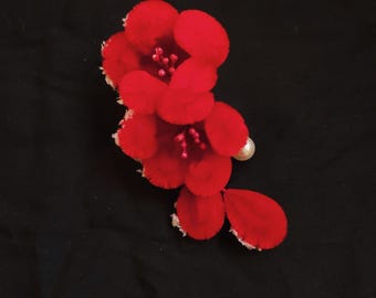 May include: A red fabric flower with a pearl accent. The flower is made of multiple layers of fabric and has a ruffled edge.