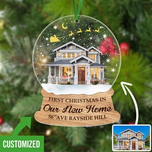 May include: A personalized Christmas ornament featuring a snow globe with a house inside. The base of the ornament is made of wood and reads "First Christmas in Our New Home 56th Ave Bayside Hill".