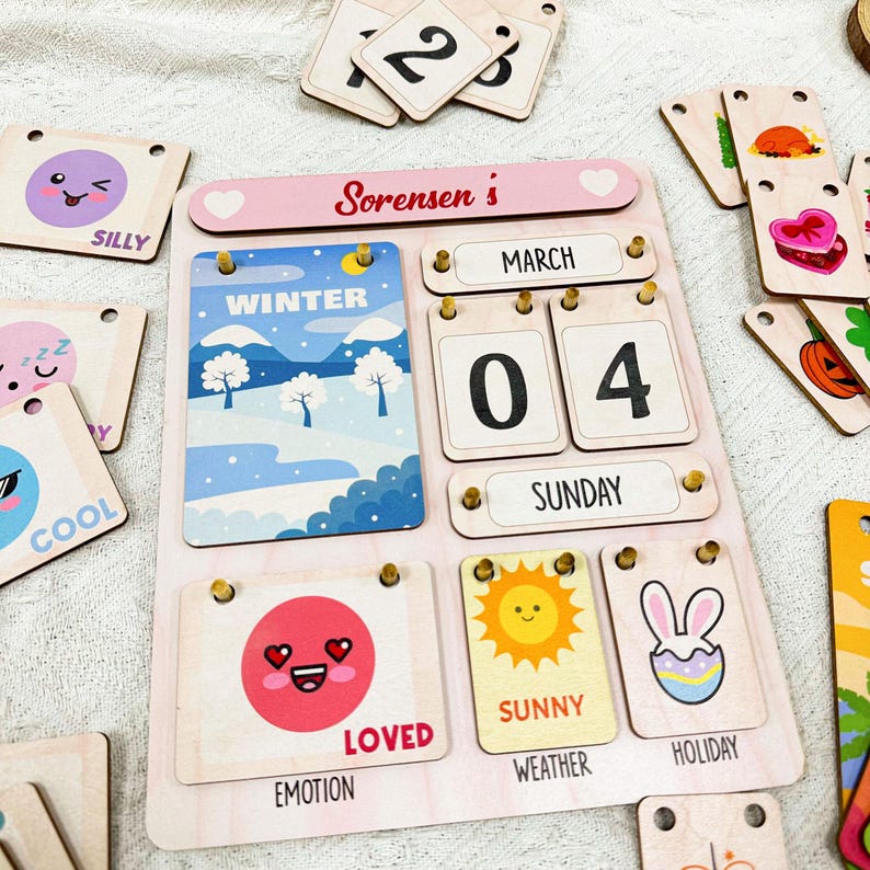 May include: A wooden calendar with a pink background and a heart at the top. The calendar says "Sorensen's" and has a date of March 4th, Sunday. The calendar also has a winter scene, a smiley face, a sun, and a bunny rabbit.