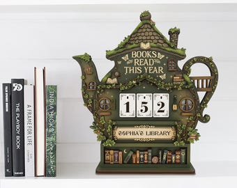 May include: A whimsical green teapot-shaped book counter with the text "BOOKS READ THIS YEAR" and the number "152". The counter has a miniature library design with a roof, windows, and a sign that reads "SOPHIA'S LIBRARY".