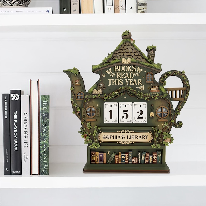 May include: A whimsical green teapot-shaped book counter with the text "BOOKS READ THIS YEAR" and the number "152". The counter has a miniature library design with a roof, windows, and a sign that reads "SOPHIA'S LIBRARY".