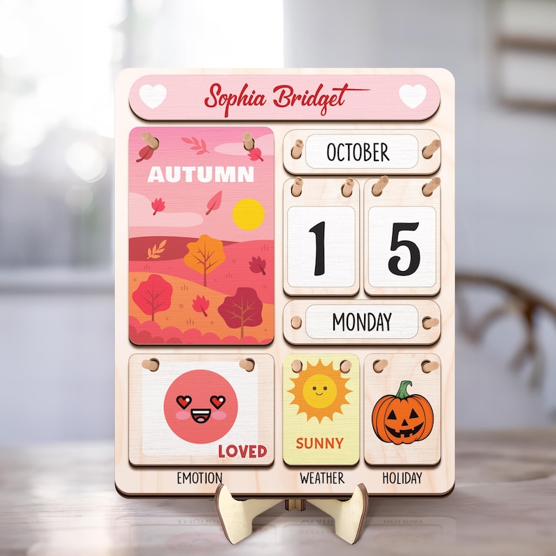 May include: A wooden calendar with a pink and red autumn theme. It features a date display, a day of the week, and icons for emotion, weather, and holiday. The calendar is personalized with the name "Sophia Bridget" and the date "October 15, Monday".