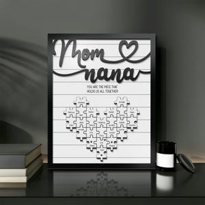 May include: Black and white framed print with the words "Mom & Nana" in a decorative font. The print features a heart-shaped puzzle with names of family members inside. The text below the puzzle reads "You are the piece that holds us all together."