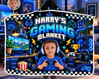 May include: A black hooded blanket featuring a white and blue pixelated design with the text HARRY'S GAMING BLANKET, a crown icon, lightning bolts, and game controllers. The centre displays a child wearing headphones and holding a controller.