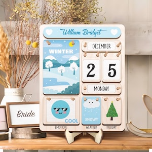 May include: A wooden calendar with a blue and white winter scene, the date December 25th, and the day of the week Monday. The calendar also has a cool emoji, a snowy cloud, and a Christmas tree.