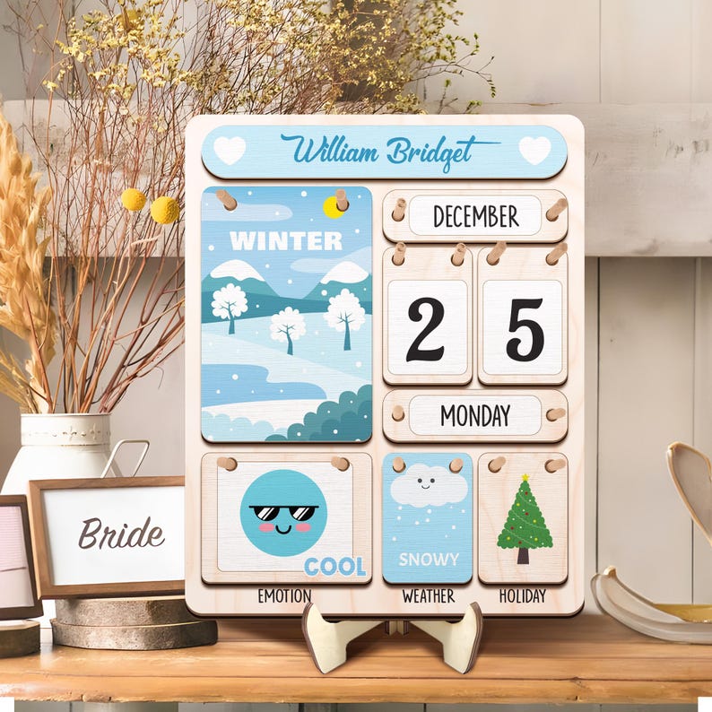 May include: A wooden calendar with a blue and white winter scene, the date December 25th, and the day of the week Monday. The calendar also has a cool emoji, a snowy cloud, and a Christmas tree.
