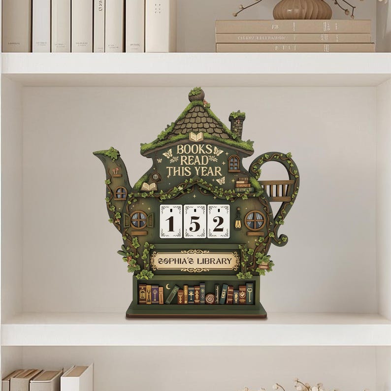 May include: A whimsical, green teapot-shaped bookshelf decor piece with the words "BOOKS READ THIS YEAR." It features a counter displaying "152" and the text "SOPHIA'S LIBRARY." The design includes miniature books and a charming, fairy-tale aesthetic.