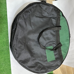 May include: A black and green round bag with a zipper and a handle. The bag has a green patch on the front.