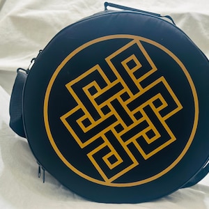 May include: A black round bag with a gold knotted design. The bag has a shoulder strap and a zipper closure.