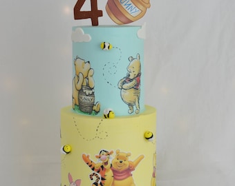 May include: A two-tiered Winnie the Pooh themed birthday cake decorated with Winnie the Pooh and Tigger characters, a honey pot, and bees. The cake is decorated with a number 4 on top.