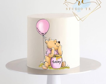 May include: A white cake decorated with a cartoon illustration of Winnie the Pooh holding a pink balloon and a honey pot. The cake is on a white cake stand. The honey pot has the word "Hunny" on it.