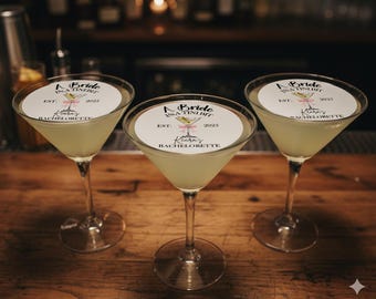 May include: Three martini glasses filled with a light green liquid, each with a circular label that reads "A Bride in a Tini Bit" and "Keara's Bachelorette" with the year 2025. The glasses sit on a wooden surface.