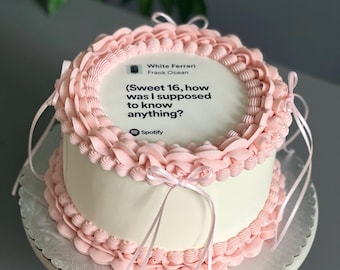 May include: A two-tiered white cake with pink frosting and ribbons. The top of the cake has the text "White Ferrari Frank Ocean (Sweet 16, how was I supposed to know anything?" and the Spotify logo.
