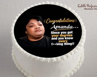 May include: A white frosted cake with a black circular image on top. The image features a woman's portrait and the text "Congratulations Amanda... Since you got your degrees and you know every f**king thing!!"