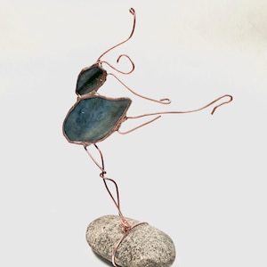 May include: A wire sculpture of a ballerina in a blue glass dress, standing on a gray stone base.