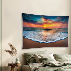 May include: A tapestry featuring a vibrant sunset over a beach with foamy waves crashing on the shore. The sky is a mix of orange, pink, and purple hues, with clouds reflecting the warm light. The waves are white and foamy, creating a contrast against the sandy beach.
