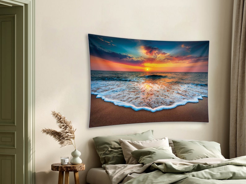 May include: A tapestry featuring a vibrant sunset over a beach with foamy waves crashing on the shore. The sky is a mix of orange, pink, and purple hues, with clouds reflecting the warm light. The waves are white and foamy, creating a contrast against the sandy beach.