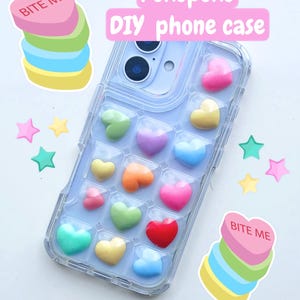 May include: A clear phone case with a light blue phone inside, decorated with colourful heart-shaped charms. The text "Pokopoko DIY phone case" is displayed in pink. Stickers with the text "Bite Me" and star shapes are also present.