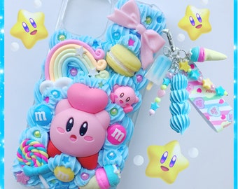 May include: A clear phone case decorated with a pink bow, a rainbow, a pink and white ice cream cone, a pink and white macaron, a pink and white swirl, a pink and white candy cane, a pink and white lollipop, a pink and white star, a pink and white M&M, a pink and white Kirby character, and a pink and white star. The case has a clear back and a white front. The case is attached to a pink and white charm with a pink and white star, a pink and white swirl, and a pink and white candy cane.