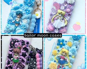 May include: Four different Sailor Moon phone cases with various designs. Each case features a different Sailor Moon character, including Sailor Moon, Sailor Mercury, Sailor Mars, and Sailor Jupiter. The cases are decorated with colorful 3D embellishments, such as flowers, stars, and hearts. The cases are all clear and show the phone screen through the back.