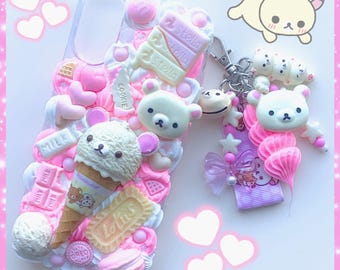 May include: A clear phone case decorated with pink and white embellishments, including bear figures, ice cream cones, and candy. A matching keychain with bear charms and a pink ribbon is attached. The overall theme is cute and kawaii.