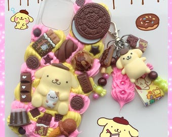 May include: A clear phone case decorated with a variety of colorful 3D embellishments, including chocolate bars, cookies, and a small yellow cartoon dog. The case also has a pink and yellow swirl design and a small charm with a yellow cartoon dog.