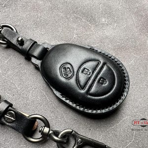 May include: Black leather key fob with two buttons. The fob is attached to a black leather keychain with a silver metal ring.