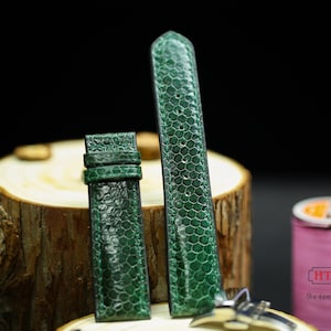 May include: Two green leather watch straps with a textured pattern. The straps are on a wooden surface.