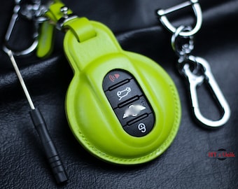 May include: A bright green leather key fob with a silver key ring and a silver carabiner. The key fob has a black button with a car icon, a black button with a lock icon, and a black button with a speaker icon.