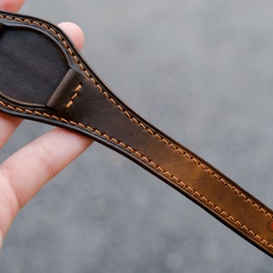 May include: A brown leather watch strap with orange stitching. The strap is designed for a watch with a round face.