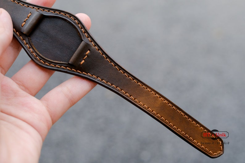 May include: A brown leather watch strap with orange stitching. The strap is designed for a watch with a round face.