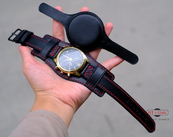 May include: A black leather watch strap with red stitching. The strap is designed to be worn around the wrist like a cuff. The watch face is gold with black hands and a black dial. The strap is attached to a separate black leather cuff that can be used to store the watch when not in use. The text "HT x Unik" is visible on the strap.