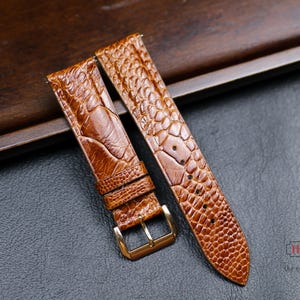 Könnte beinhalten: Zwei braune Lederarmbänder mit Krokodilmuster. Die Armbänder liegen auf einer braunen Holzoberfläche.