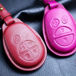 May include: Two leather key covers, one red and one pink, with button impressions. The covers are designed to fit a car key fob.