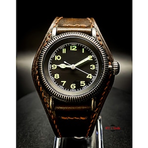May include: A black watch with a brown leather strap and a black face with white numerals. The watch has a luminous dial with a white second hand.